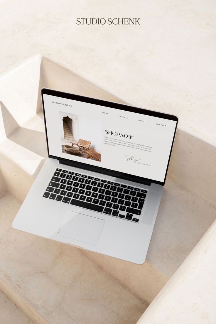 Laptop on steps displaying website with minimalist design and text 'Shop Now'.